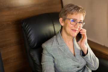 adult woman with a short haircut in a suit sits in the chair of a private plane with a phone in her hands