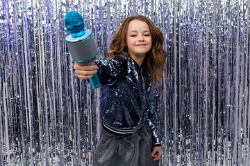 Obraz premium funny beautiful holiday host holds out a microphone and shows the class against a background of shiny tinsel