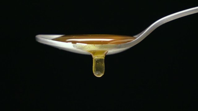 Slow motion shot : Close up honey dripping on the stainless tea spoon on black back ground.