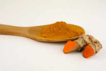 Turmeric powder in a wooden spoon and cross root on a white background. Used as a tonic for body...