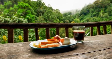 Obraz premium Breakfast and blackcoffee at balcony with forest and mountain scenery in morning, Chiangmai, Thailand