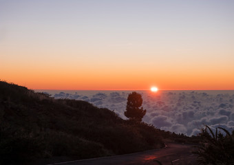 Beautiful red sunset above white clouds cover with sun rays and asphalt road at mountains at La Palma, Canary Island, Spain