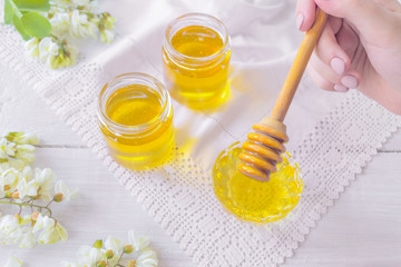 jars of fresh honey and a honey stick on the table. honey stick in hand and jars of acacia honey close-up.