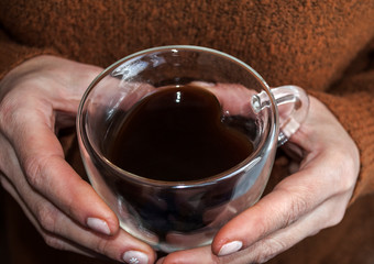 Glass cup in the shape of a heart and double glass in female hands. A cup of coffee.