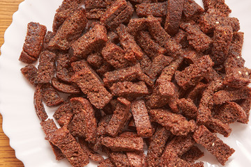 Sliced in cubes dark bread pieces crackers in a white plate top view close up background. Bread texture. Bread backdrop on wooden table.