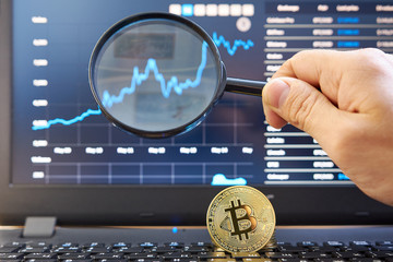 In a laptop, the display shows the Bitcoin exchange and the expert chart the price movement through a magnifier looks at a chart of Japanese candles