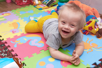Fototapeta na wymiar Closeup of happy smiling baby boy crawling on colorful playmat. child on a play mat with toys. smiling child with down syndrome.