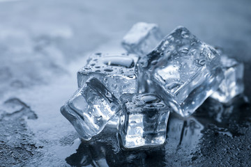 Crystal clear ice cubes with water drops on grey table, closeup