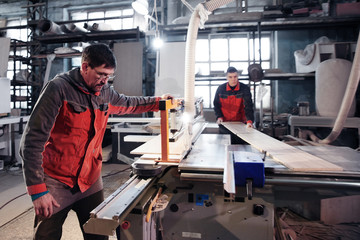 Fototapeta premium Process of production and manufacture of wooden furniture in furniture factory. Worker carpenter man in overalls processes wood on special equipment