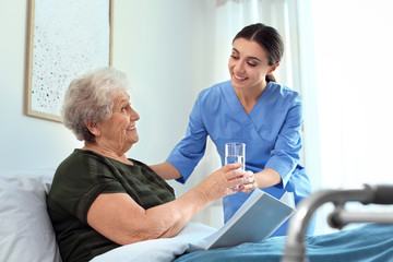 Care worker giving water to elderly woman in geriatric hospice