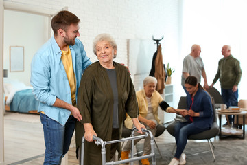 Care worker helping to elderly woman with walker in geriatric hospice