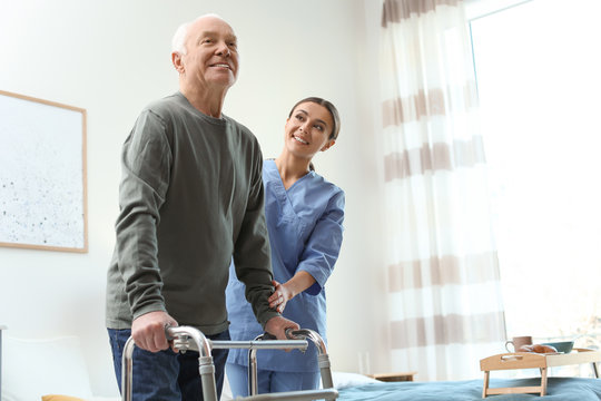 Care Worker Helping Elderly Man With Walker In Geriatric Hospice