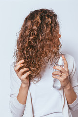 Young woman applying moisturizing spray to her curly hair