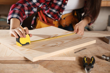 Female carpenter measuring wooden board in workshop, closeup