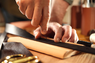 Man making holes in leather belt with stitching awl at table, closeup