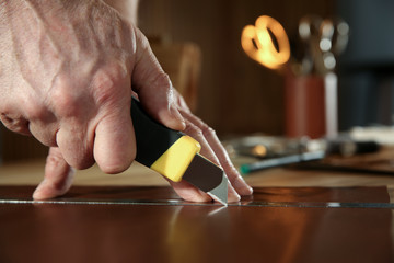 Man cutting leather with knife in workshop, closeup