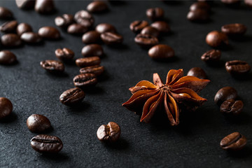 Star anise and roasted coffee beans scattered on a black textured stone surface. Low key image of coffee drink ingredients.