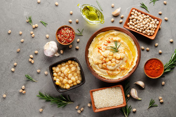 Hummus topped with chickpeas, olive oil and green coriander leaves on stone table with different spices aside. Flat lay
