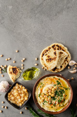 Flat lay view at Hummus in clay dish topped with olive oil, chickpeas and green coriander leaves on stone table served with traditional Pita bread