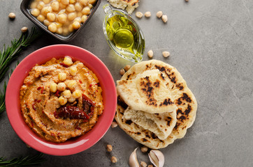 Flat lay view at Hummus in clay dish topped with olive oil, chickpeas and sun dried tomatoes on stone table served with traditional Pita bread