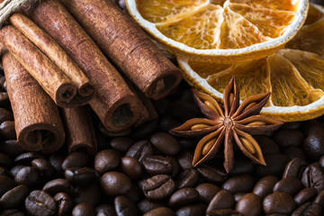 Cinnamon sticks, dried orange and star anise on a roasted coffee beans background. Low key image of coffee drink ingredients.