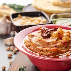 Fresh homemade Hummus in clay dish topped with olive oil, chickpeas, spices and sun dried tomatoes on stone table