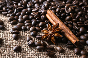 Star anise and cinnamon stick on a roasted coffee beans over a sackcloth background. Low key image of coffee drink ingredients.