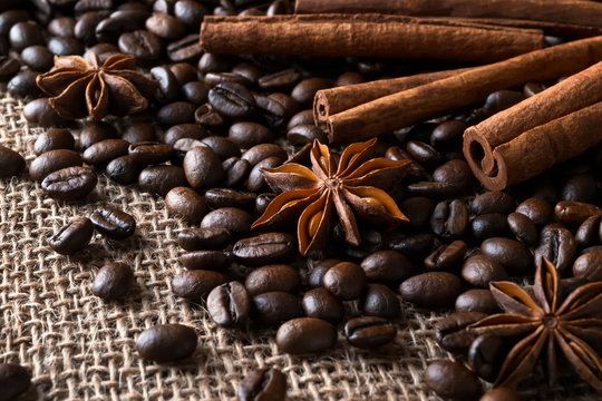 Cinnamon sticks and star anise on a roasted coffee beans over a sackcloth background. Low key image of coffee drink ingredients.