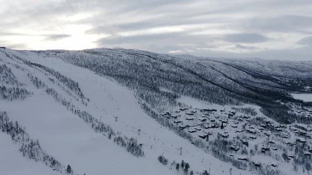 Aerial view above Geilo  snowy mountain ski resort town settlement buildings at base of rocky mountain ridge landscape.