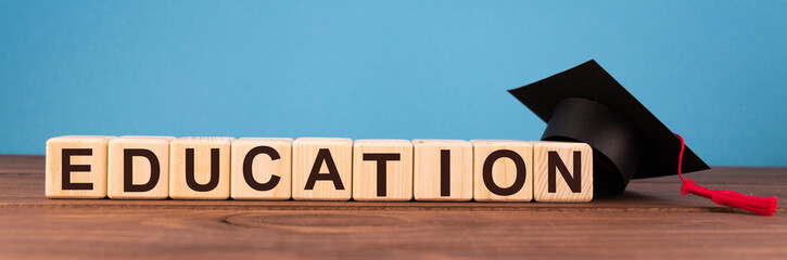 Word Education on wooden cube blocks on wood table with a graduation hat on blue background. Financial, education, business or economic concept.