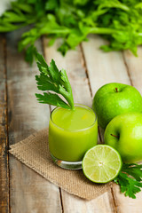 Healthy food, vegan diet concept - glass of fresh green juice or smoothie with celery, apple, orange. Antioxidant fresh detox beverage with raw ingredients.  Close up, wooden background