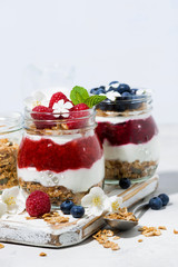desserts with muesli, berry and fruit puree in jars on white table, vertical