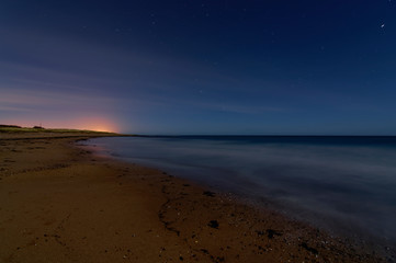 A long exposure night photograph of Easthaven beach with the tide out, and the lights of Arbroath seen above the horizon on a December Night.