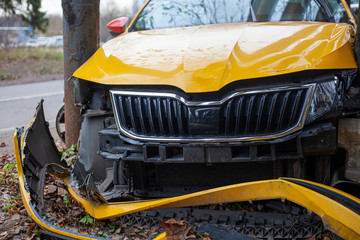 A taxi car crashed into a pole. A yellow car flew off the road. Car accident. Dangerous situation. The car frame is broken. Crumpled hood and broken wheels. The result of drunk driving.