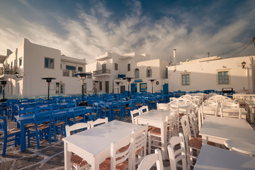 Cafe and restaurants at amazing narrow street of popular destination on Paros island. Greece. Traditional architecture and colors of mediterranean city at sunrise. Calm morning at romantic destination