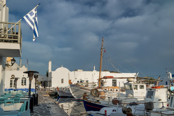 Panoramic view of Paros island. Greece. Beautiful harbor at Aegean sea, Greek flag fluttering on wind. Amazing mediterranean landscape with buildings, boats and yachts in quay at calm morning