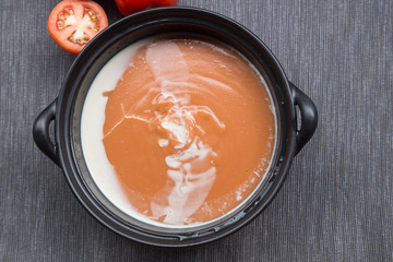 Tomato soup in a black bowl on grey background/Delicious tomato soup with aromatic spices on the table/ Top view of a bowl with tomato soup/