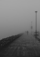 Figure walking along the pavement along the coast, on a very foggy morning. Taken on Salthill Promenade in Galway, Ireland in black and white.