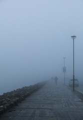 Figures walking along a coastal pavement on a very foggy day. Taken on Salthill Promenade, in Galway Ireland
