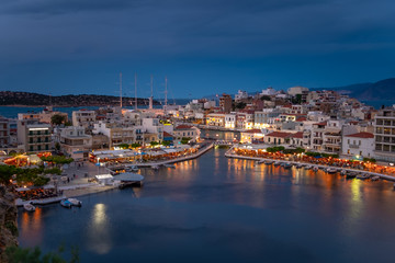 Beautiful sunset at Agios Nikolaos city, Port at Aegean sea. Crete,Greece. Peaceful harbor of Voulismeni Lake. Long promenade with restaurants.  Panoramic view of seaport with yachts and boats at quay