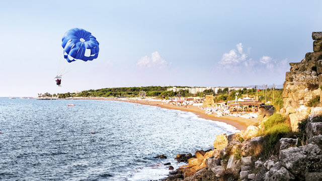 Two people parasailing on a blue parachute over the coast of Side, Turkey