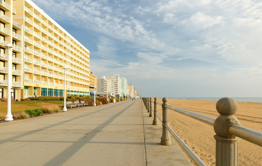 Virginia Beach at Sunrise. Photo shows hotels along the boardwalk and sand beach. The beach...