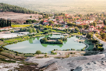 Beautiful view of Pamukkale. Cotton Castle. Limestone white Pamukkale cascade in foreground. Green geothermal lake with island and blue thermal water pool , Turkey