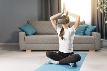 Athletic young beautiful woman sitting in padmasana with her hands raised and VR headset on