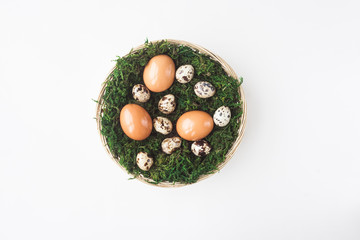 Easter.Chicken eggs and quail eggs lie in a basket with moss on a white background, top view....