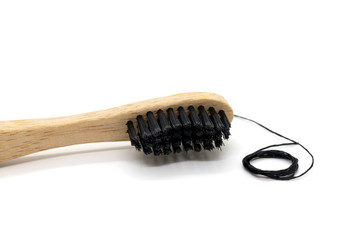 Black dental floss and bamboo toothbrush on a white background.