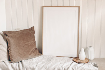 Portrait empty wooden frame mockup with linen cloth, velvet cushions and modern ceramic vases. White beadboard wainscot wall paneling background. Scandinavian interior, home design. Art concept.