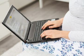 A pregnant woman uses a laptop. Hand and a notebook close-up. Concept of modern technologies and freelance. Top view