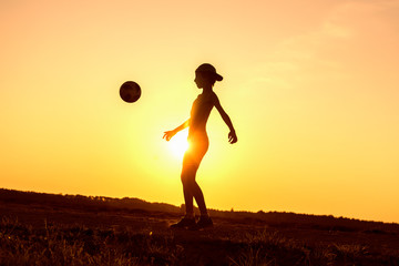 Boy playing with ball in nature in hot evening, silhouette of playing child at sunset in countryside