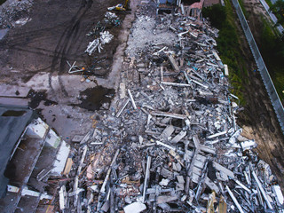 A process of buliding demolition, demolition site with heavy bulldozer and excavator with crushing equipment at work, demolished house, shot from air with drone